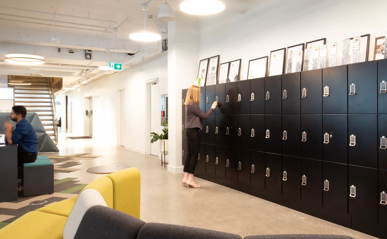 image of black digital lockers in a corporate office with a woman standing at a locker